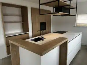 Overzicht van maatwerk keuken met wit kookeiland, houten nis en zwarte accenten