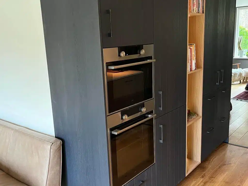 Op maat gemaakte keukenkast in Drachten met zwarte fronten, open nis met verlichting en geïntegreerde oven.